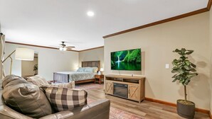 Een woonkamer met een bank, een bed, een televisie, een plafondventilator en een potplant.