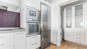 Una cocina moderna con armarios blancos, un refrigerador de acero inoxidable, un horno y un microondas.