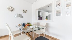 Una cocina moderna con armarios blancos, una mesa de comedor de vidrio y vista al área de estar contigua.
