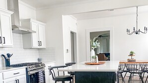 Una cocina moderna con armarios blancos, una isla central y una zona de comedor con mesa y sillas de madera.