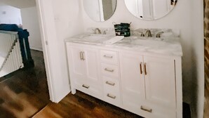 Un baño con tocador blanco, dos espejos redondos y un lavabo blanco.