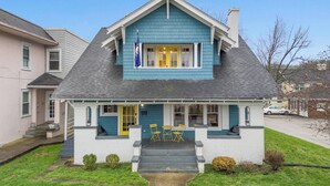 Ein zweistöckiges Haus mit Satteldach, einer Veranda mit gelben Türen und einem kleinen Vorgarten.
