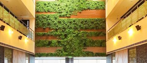 A hotel lobby with a central seating area, a green wall with plants, and a modern ceiling design.