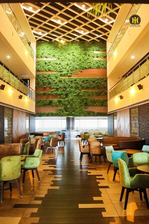 A hotel lobby with a central seating area, a green wall with plants, and a modern ceiling design. - Ranjitha Palace (Manipal Inn) (Udupi)