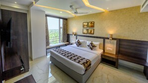 A modern hotel room with a large bed, a TV, a window with a view, and a ceiling fan. - Ranjitha Palace (Manipal Inn) (Udupi)