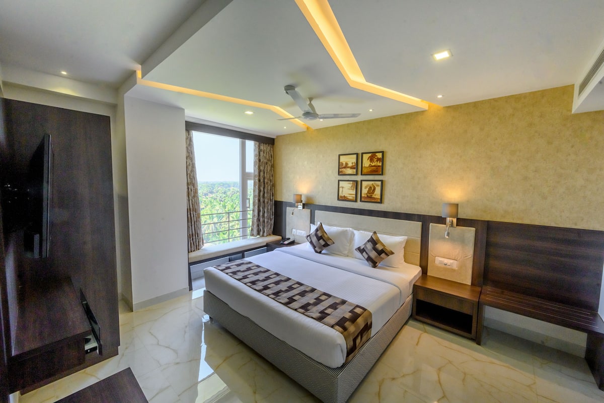 A modern hotel room with a large bed, a TV, a window with a view, and a ceiling fan.