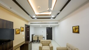 A modern living room with a flat-screen TV, a ceiling fan, and a dining area with chairs and a table. - Ranjitha Palace (Manipal Inn) (Udupi)