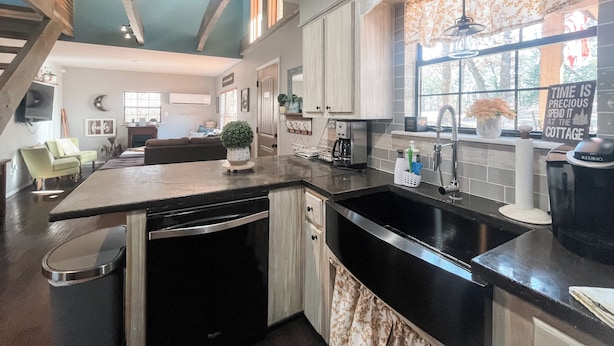A modern kitchen with a black countertop, stainless steel appliances, and a window with a view of trees. - Wister Ridge Cottage • Sleeps 10 • 3 Minutes to Wister Lake! (Wister)