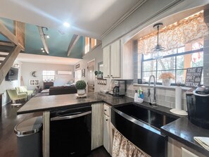 A modern kitchen with a black countertop, stainless steel appliances, and a window with a view of trees. - Wister Ridge Cottage • Sleeps 10 • 3 Minutes to Wister Lake! (Wister)