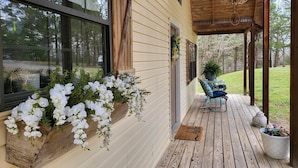 A wooden deck with a covered porch, a large window, and a hanging flower planter. - Wister Ridge Cottage • Sleeps 10 • 3 Minutes to Wister Lake! (Wister)