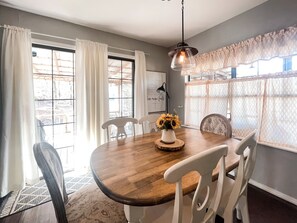 A dining area with a wooden table, white chairs, a vase with sunflowers, and a pendant light. - Wister Ridge Cottage • Sleeps 10 • 3 Minutes to Wister Lake! (Wister)