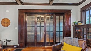 Ein Zimmer mit Holzboden, einem Ledersessel mit gelbem Kissen, einer Holztür mit Glasfeldern und einem Schrank mit Glastüren.