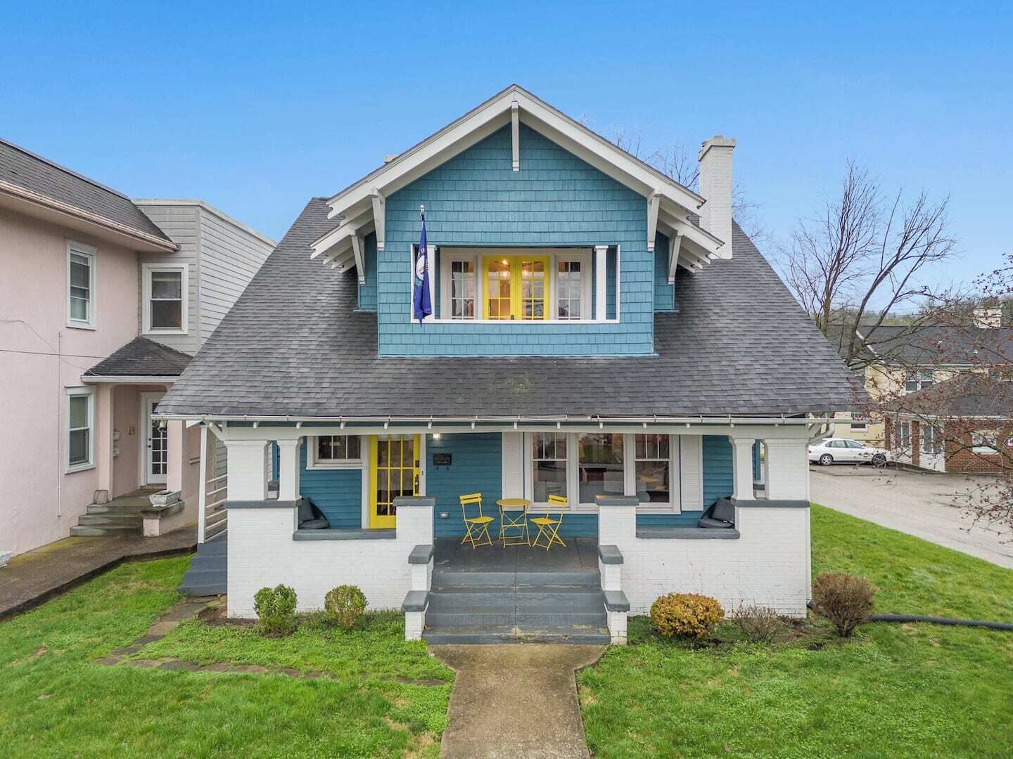 Une maison à deux étages, dotée d’un toit à pignon, d’un porche avec des portes jaunes et d’un petit jardin devant.