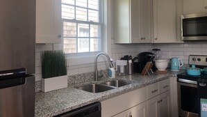 Une cuisine moderne avec des meubles blancs, un plan de travail en granit, des appareils électroménagers en acier inoxydable et une fenêtre qui laisse entrer la lumière naturelle.