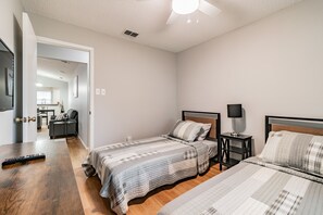 Un dormitorio con dos camas, una mesa de madera, una mesita de noche y un ventilador de techo.