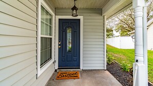 A house with a dark blue front door, a white porch, and a doormat that reads "Home Sweet Home". - Entire House with Game Room in Lutz, Near Tampa and Wesley Chapel (Lutz)