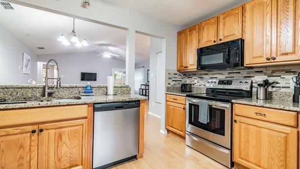 A modern kitchen with wooden cabinets, granite countertops, stainless steel appliances, and a dishwasher. - Entire House with Game Room in Lutz, Near Tampa and Wesley Chapel (Lutz)