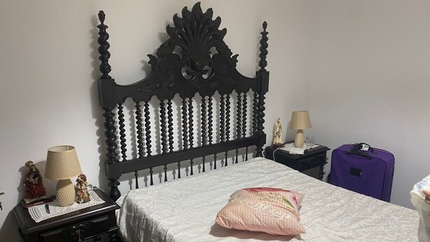 Un dormitorio con cama, mesita de noche, cómoda, lámpara, estatua y maleta.