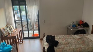 Un dormitorio con cama, escritorio, silla, una mesa con imágenes y un ventanal corredizo al exterior.