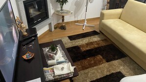 Una sala de estar con un sofá, un televisor, una chimenea, un ventilador y una mesa con varios objetos.