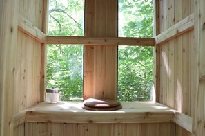 Ein Holzkamin mit Blick auf Bäume, ein hölzerner Hocker und ein Glasbehälter.