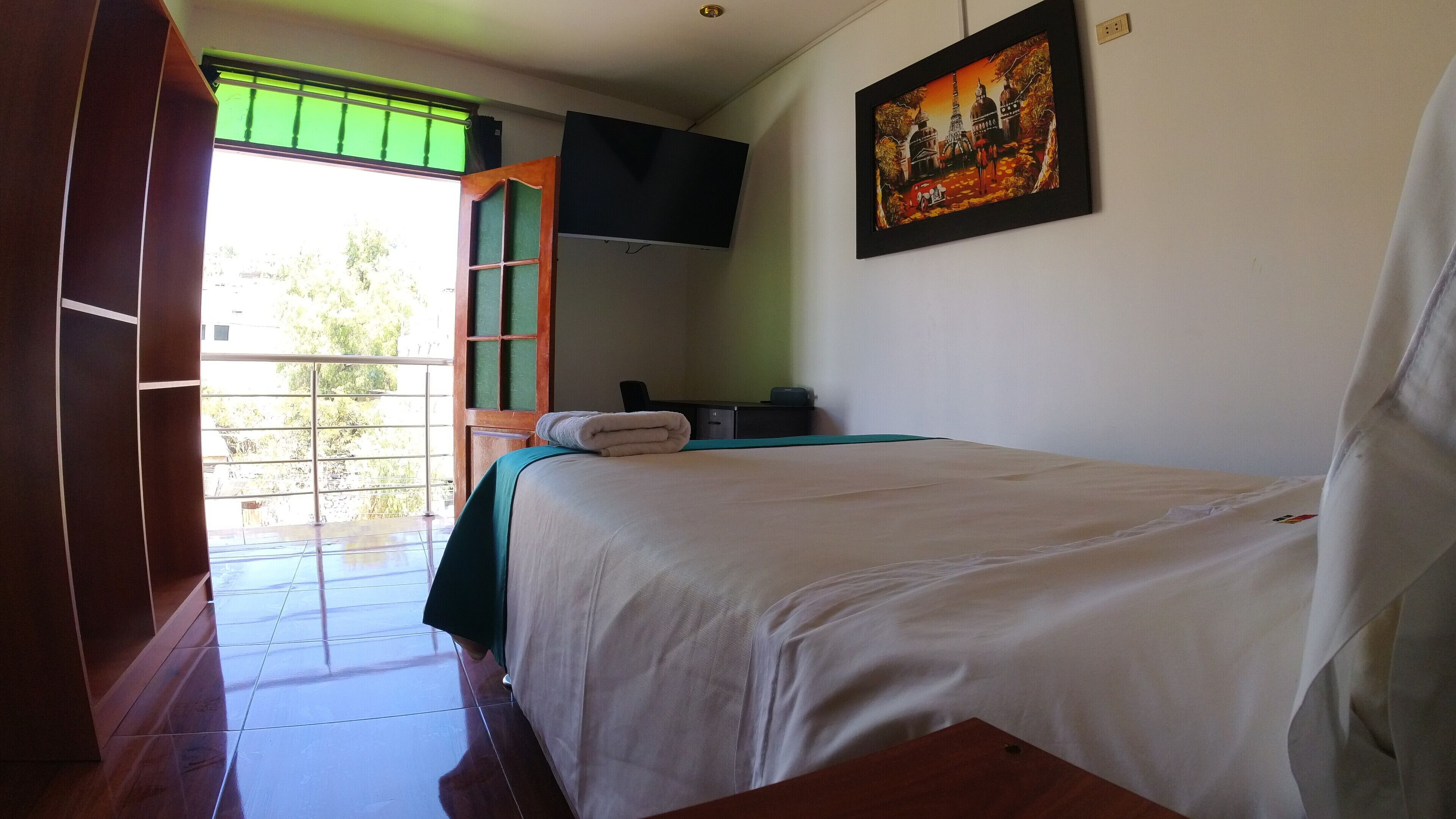 A hotel room with a bed, a desk, a chair, a window with a view, and a painting on the wall.