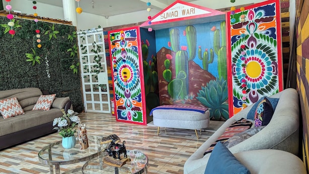 A vibrant hotel lobby with a colorful mural, a sofa, a coffee table, and a decorative cactus plant. - Sumaq Wari Hotel (Ayacucho)
