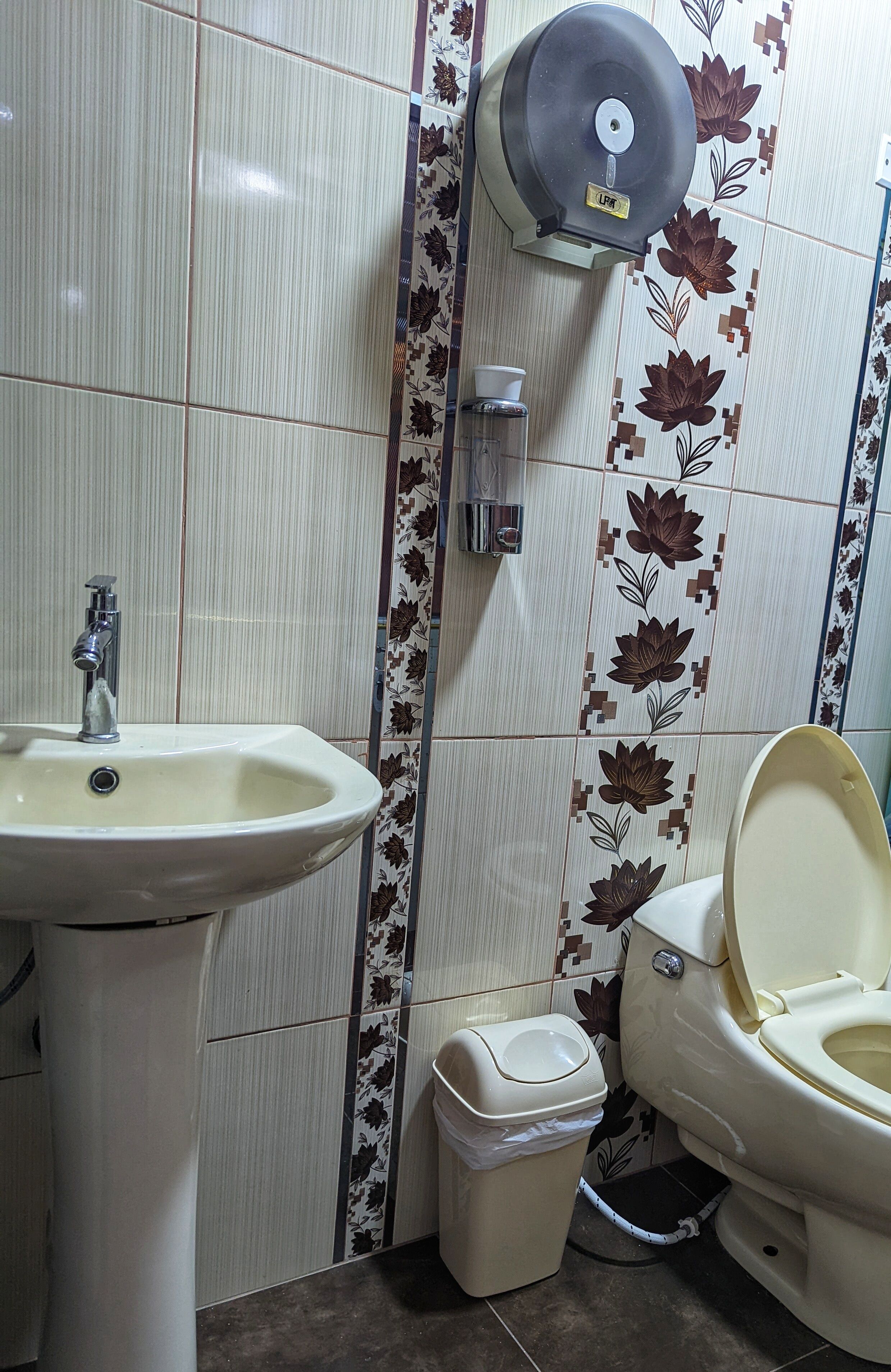 Een badkamer met een wastafel, toilet, prullenbak en handdroger.