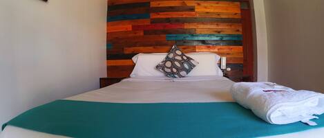 Una cama bien tendida con un edredón color turquesa y una almohada blanca con un diseño geométrico.