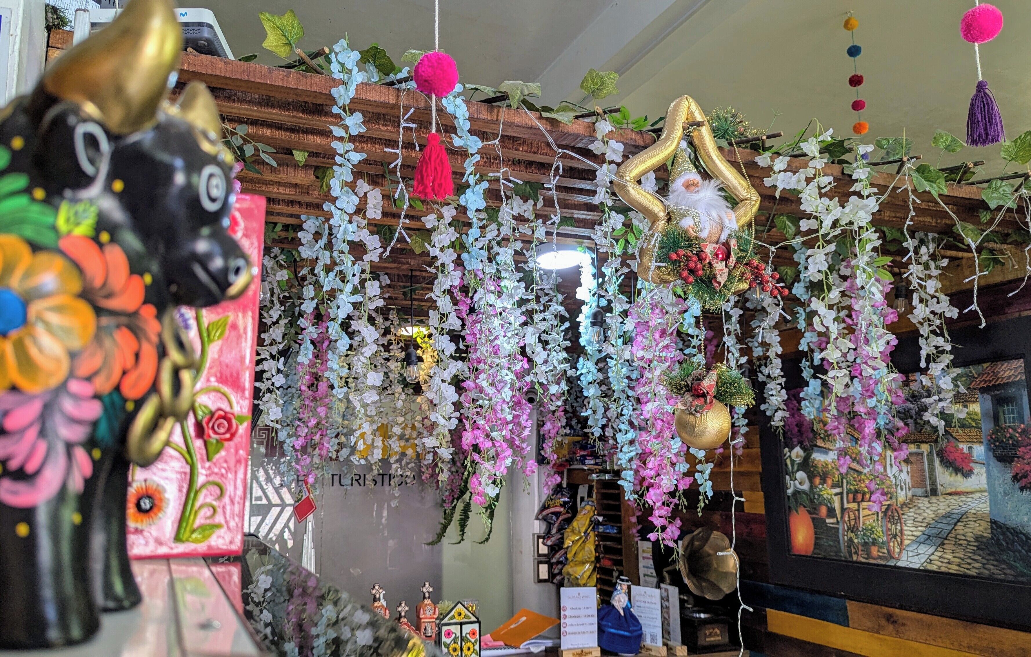A room with a wooden ceiling, hanging floral decorations, and a framed picture of a village scene.
