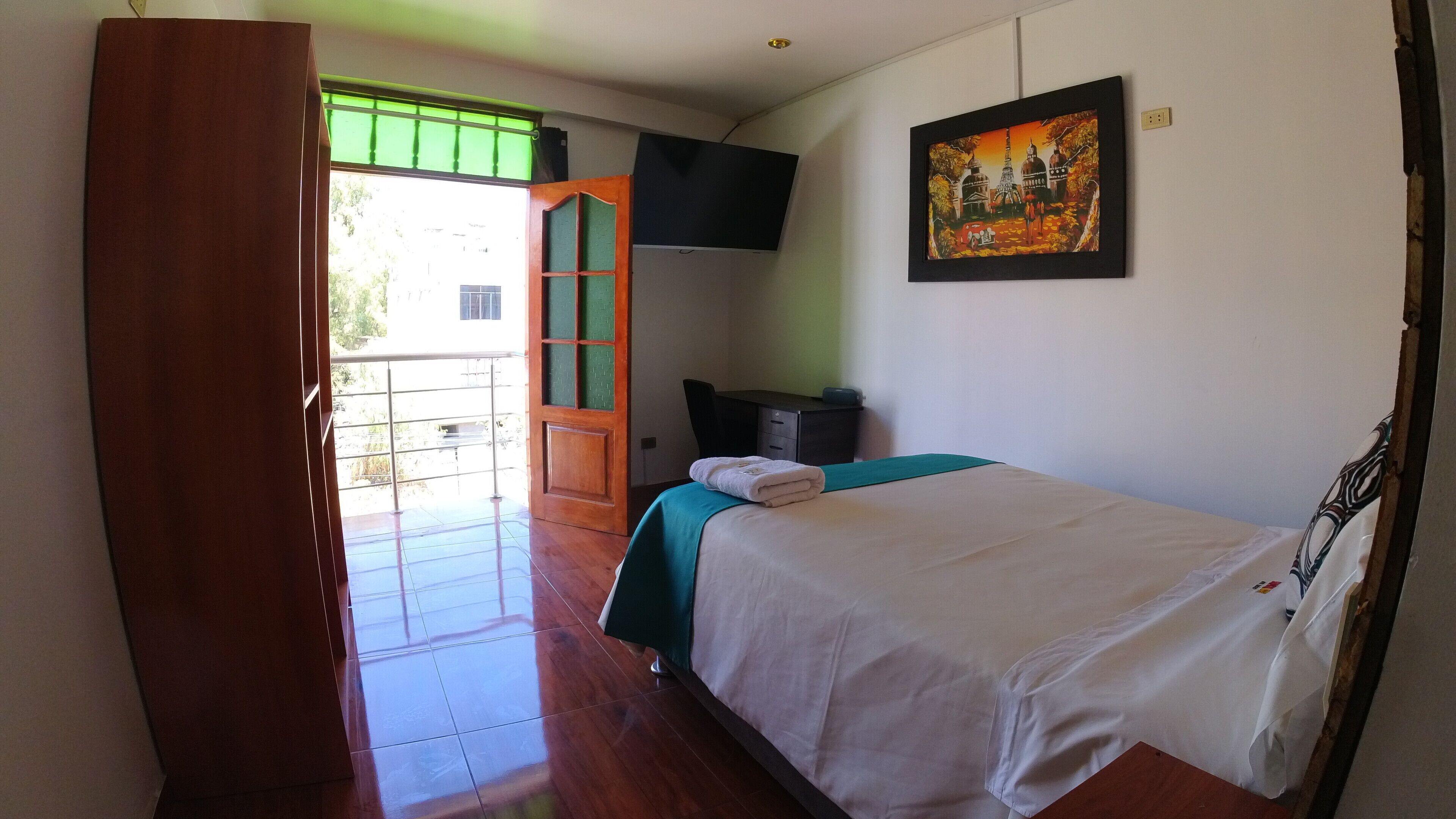 A room with a bed, a desk, a chair, a TV, and a painting on the wall.