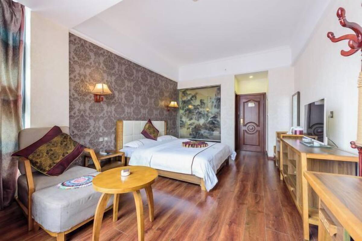 A hotel room with a bed, a sofa, a small table, a TV, and a wooden desk.