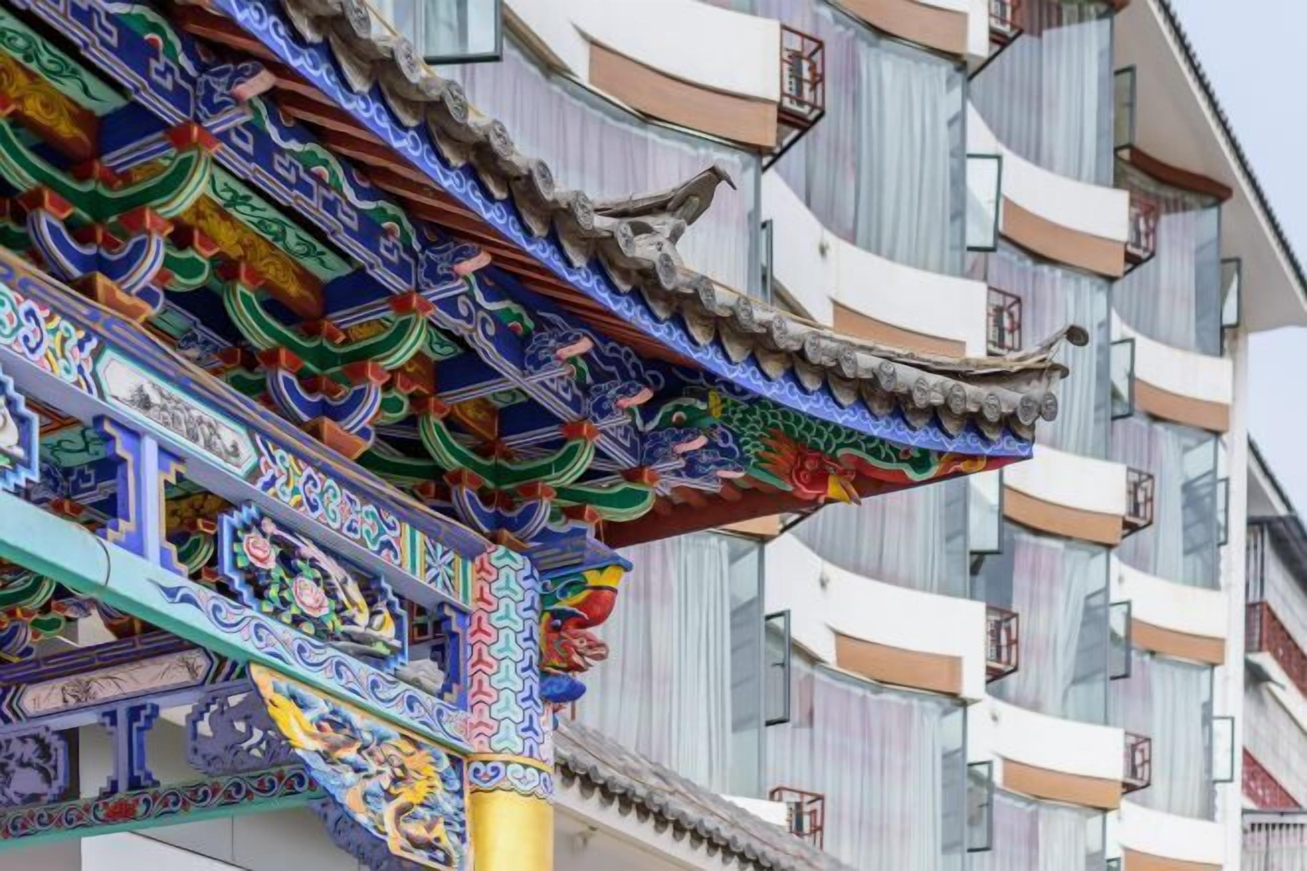 A traditional Chinese building with ornate, colorful roof decorations and a modern building adjacent to it.