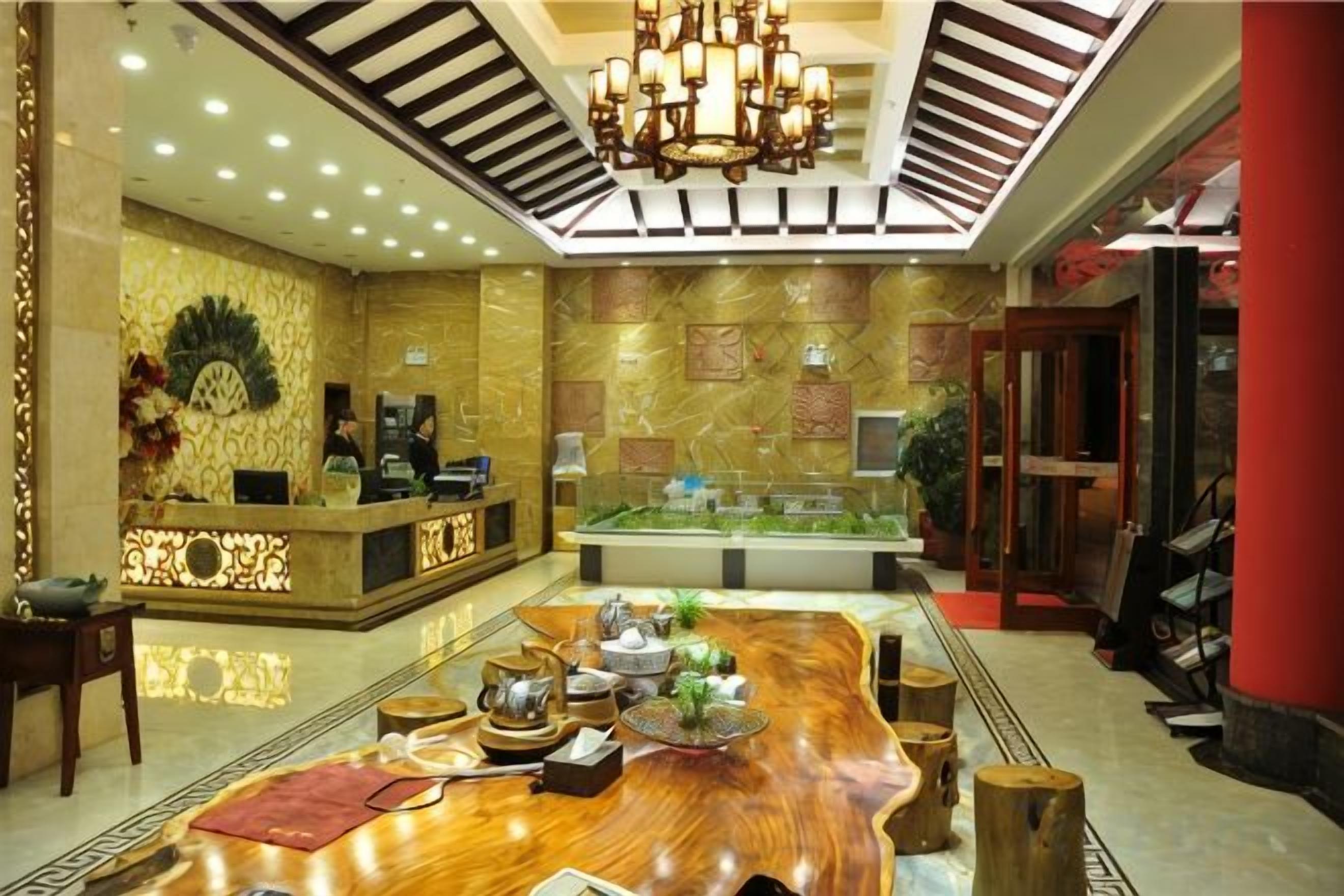 A hotel lobby with a reception desk, a large wooden dining table, and a chandelier.