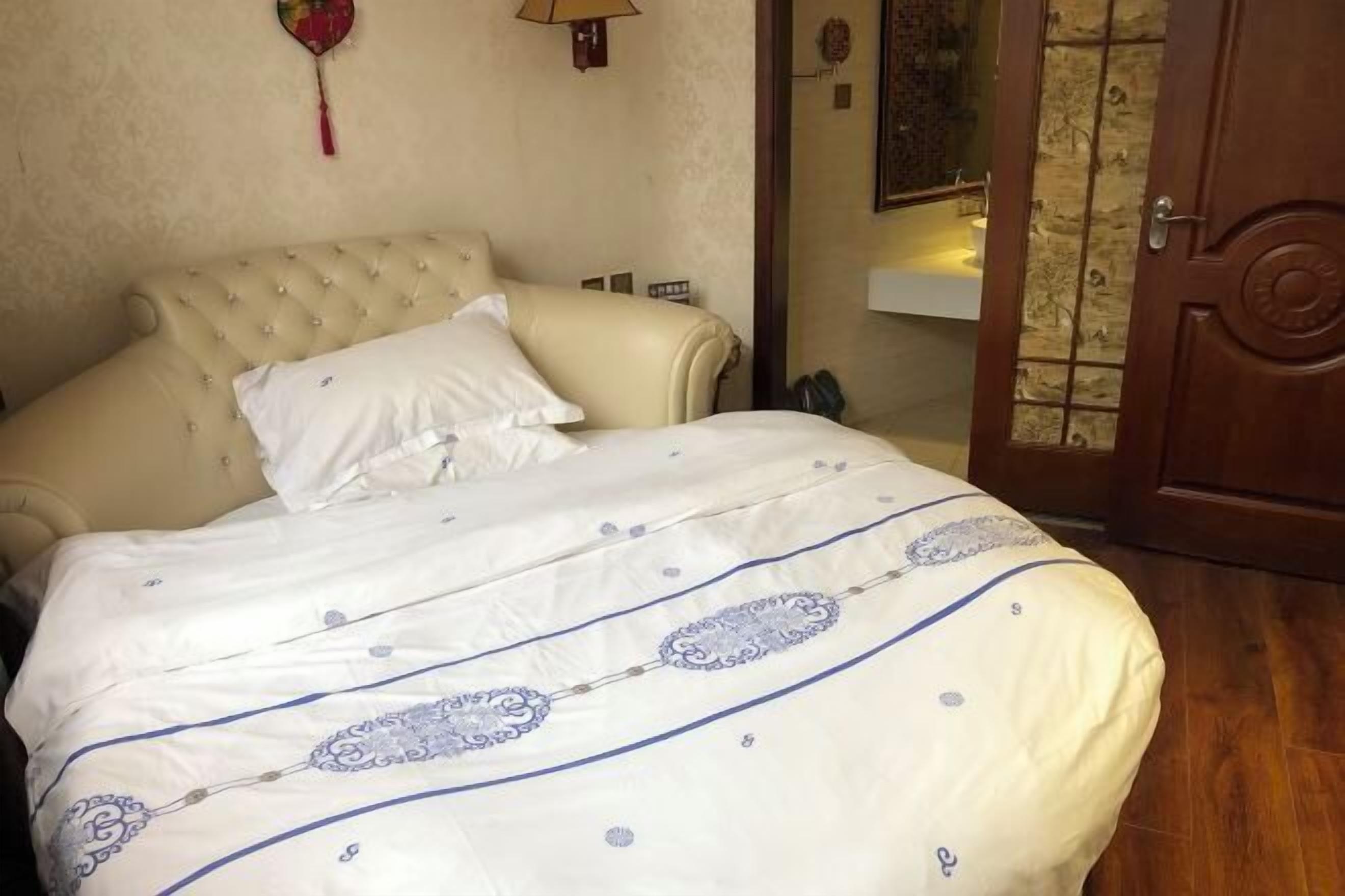 Una cama con un edredón blanco y azul estampado, un cabecero capitonado y una puerta de madera con un panel de vidrio.