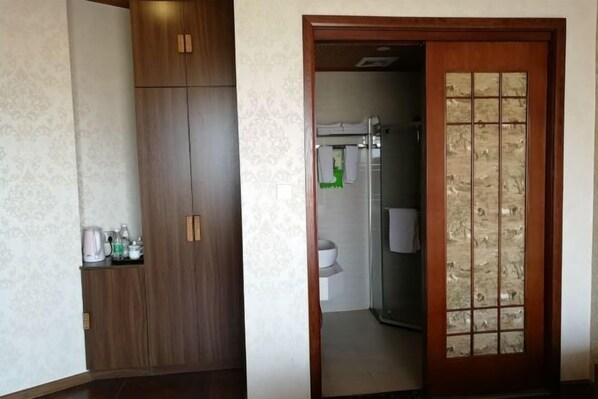 Una habitación con un armario de madera, una puerta de cristal con diseño de cuadrícula y una vista parcial de un baño con una toalla colgada.