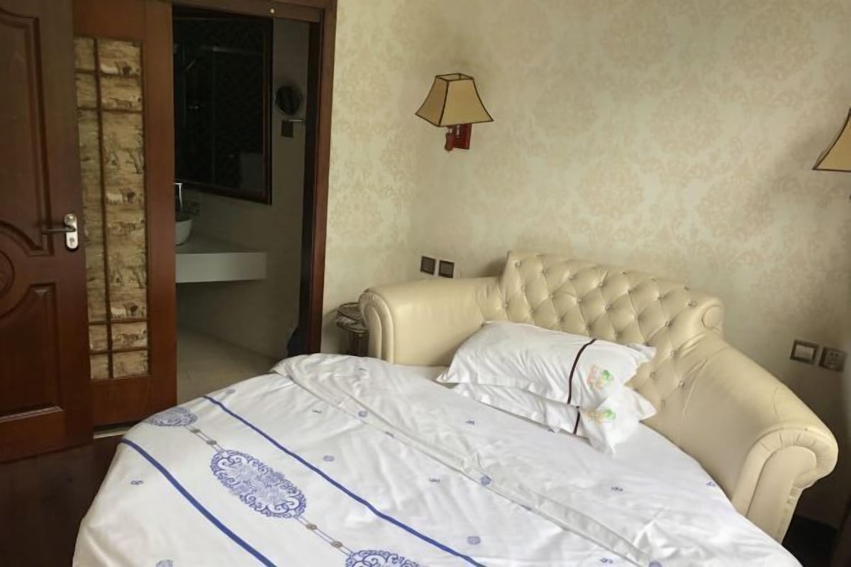 Un dormitorio con una cama grande, una puerta de madera, un baño con lavamanos y una lámpara de pared.