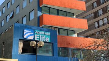 Un edificio con fachada azul y balcones anaranjados, que muestra un letrero que dice 'ApartHotel Elite'.
