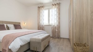 A bedroom with a bed, a bedside table, a window with curtains, a wardrobe, and a wicker basket. - Private Pool with Relaxing Nature View - Apt Mirna (Ripenda Verbanci)