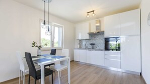 A modern kitchen with white cabinets, a black stove, and a dining area with a glass table and chairs. - Private Pool with Relaxing Nature View - Apt Mirna (Ripenda Verbanci)