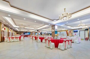Un salón de banquetes con mesas redondas, candelabros y un escenario.