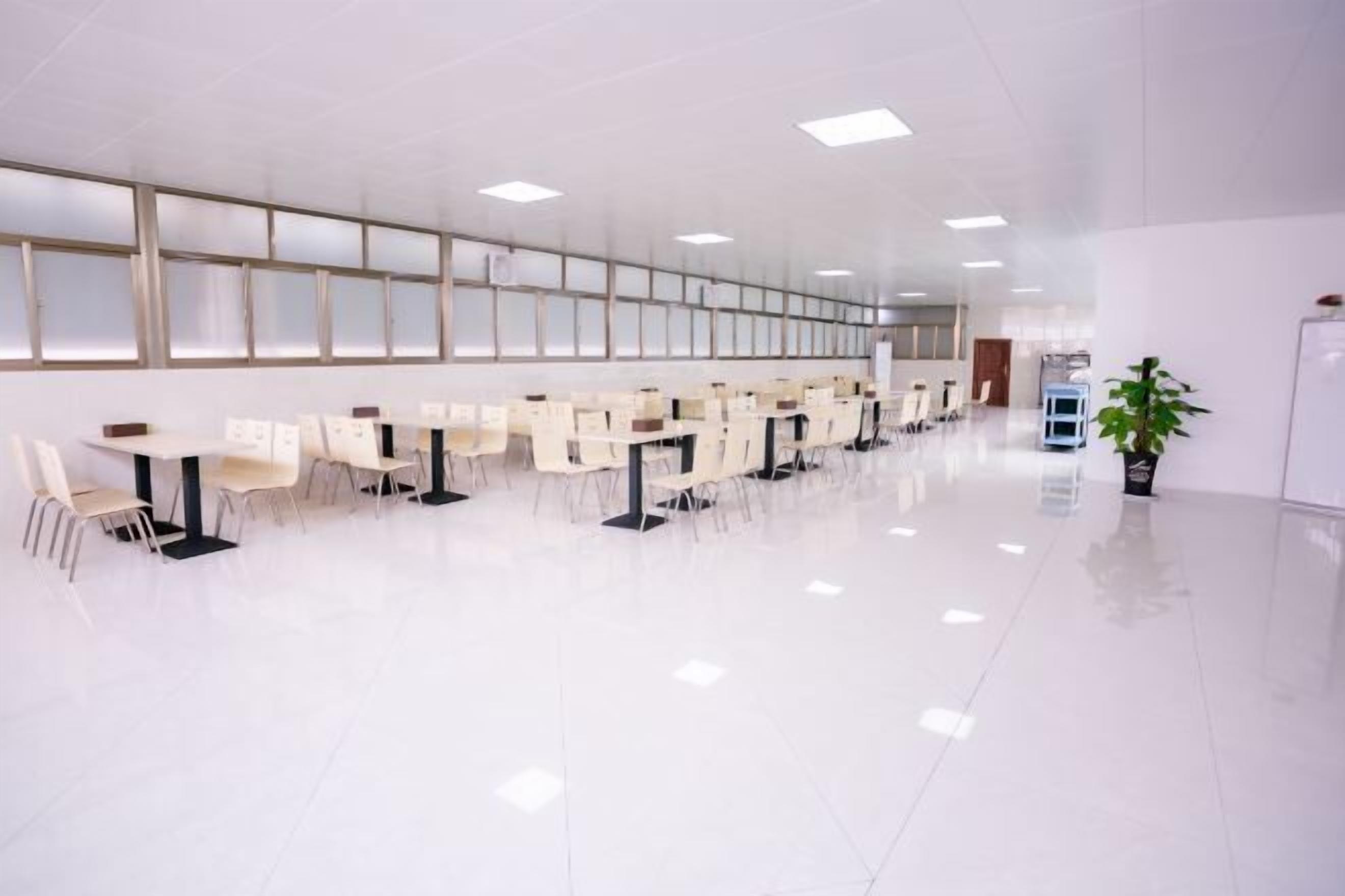 A spacious, modern conference room with rows of white tables and chairs, large windows, and a clean, polished floor.