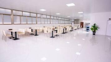 A spacious, modern conference room with rows of white tables and chairs, large windows, and a clean, polished floor.