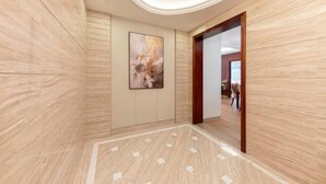 Un couloir avec un plancher en bois, un tableau accroché au mur et une porte en bois donnant sur une autre pièce.