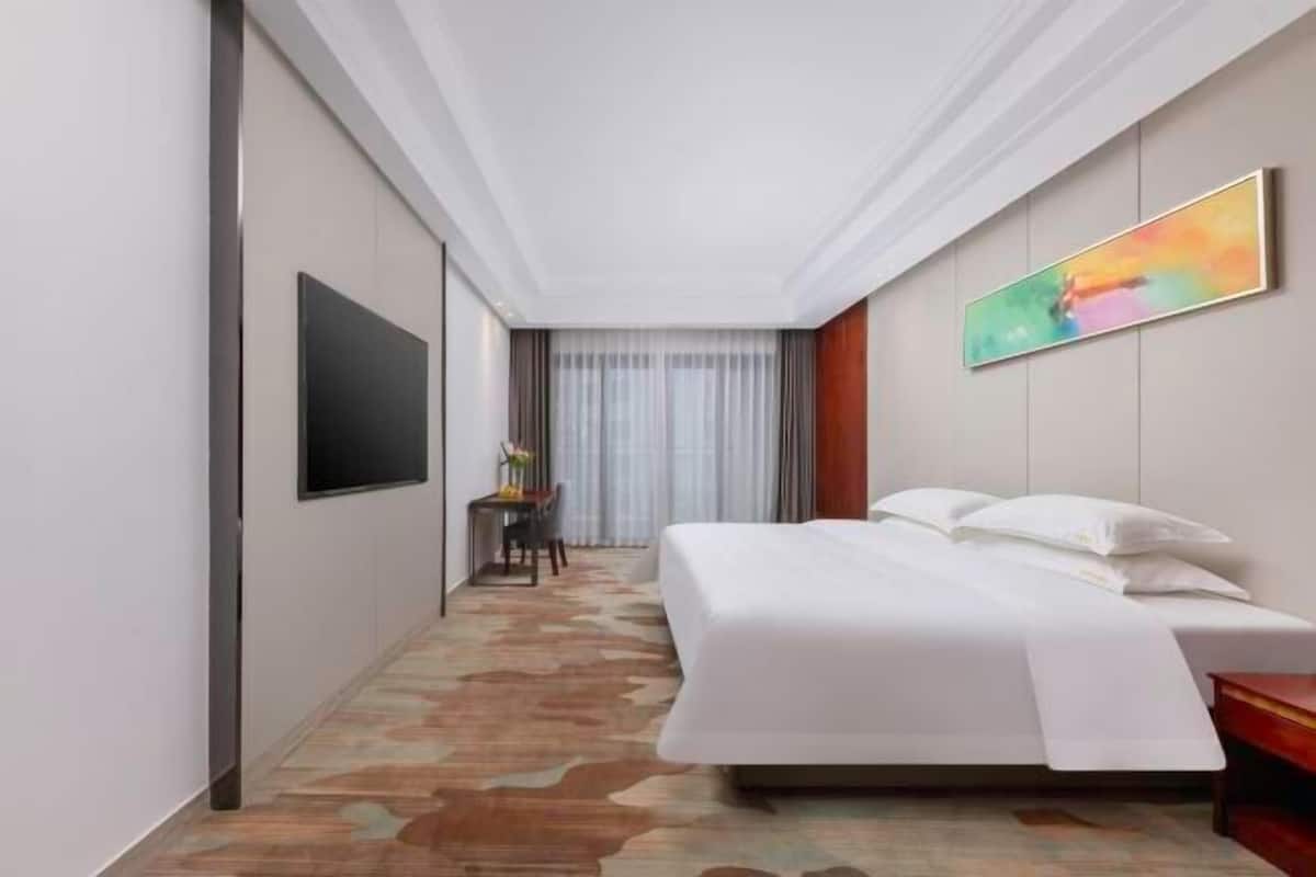 A hotel room with a large bed, a flat-screen TV, a desk with a chair, and a painting on the wall.