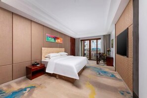 A hotel room with a large bed, a bedside table, a TV, and a view of the outside balcony.