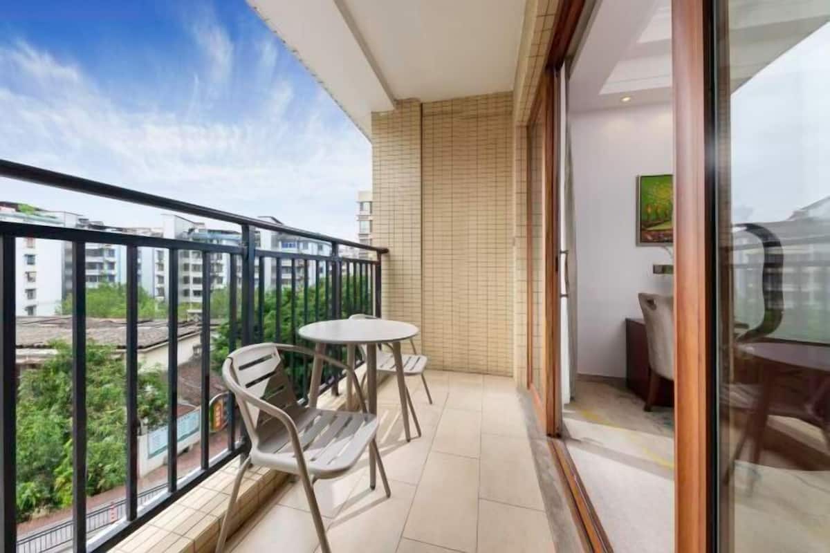A balcony with a view of buildings and greenery, a tiled floor, and a table with chairs.