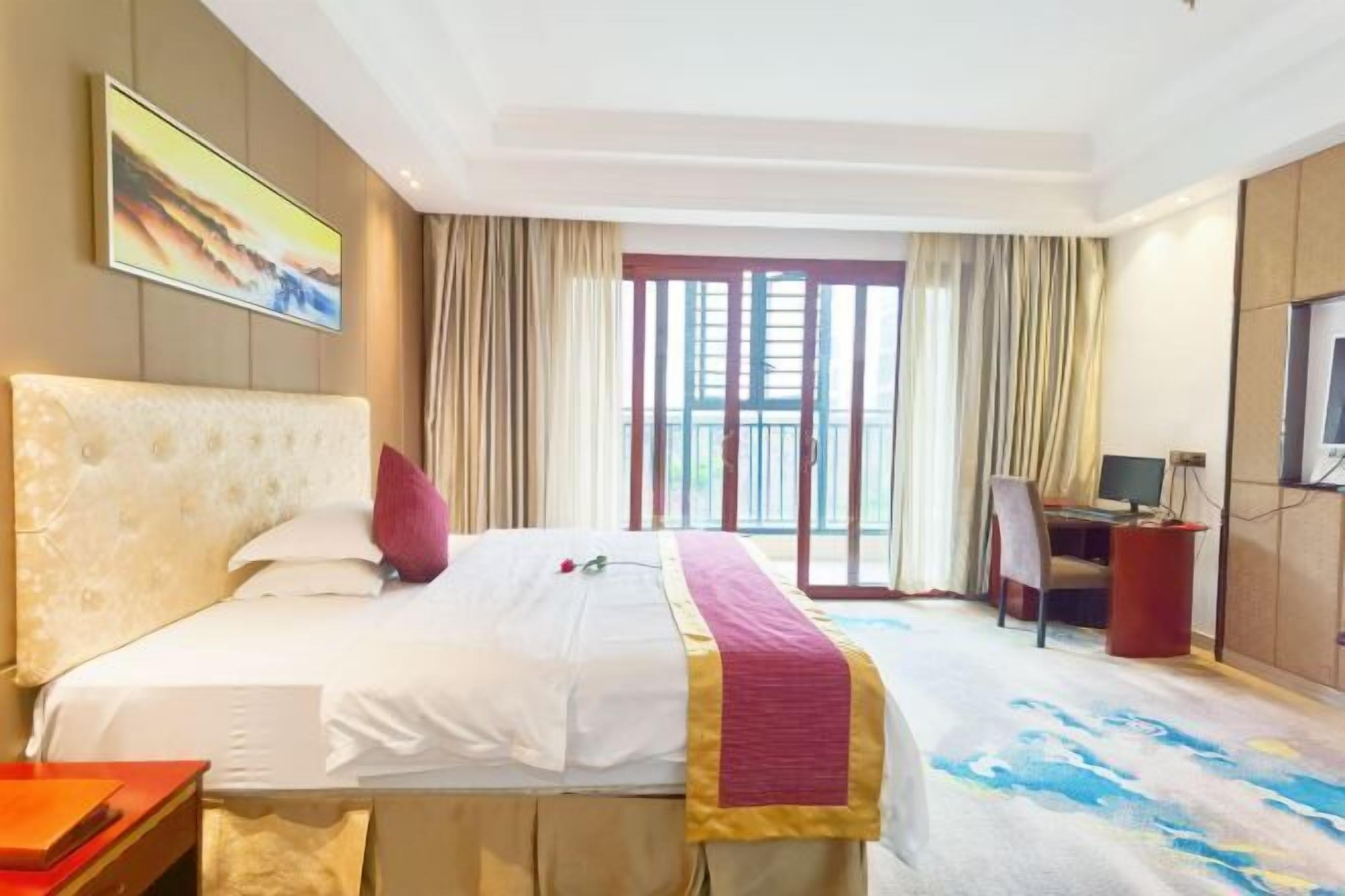 Habitación de hotel con una cama grande, un escritorio con computadora, televisión y balcón con cortinas.
