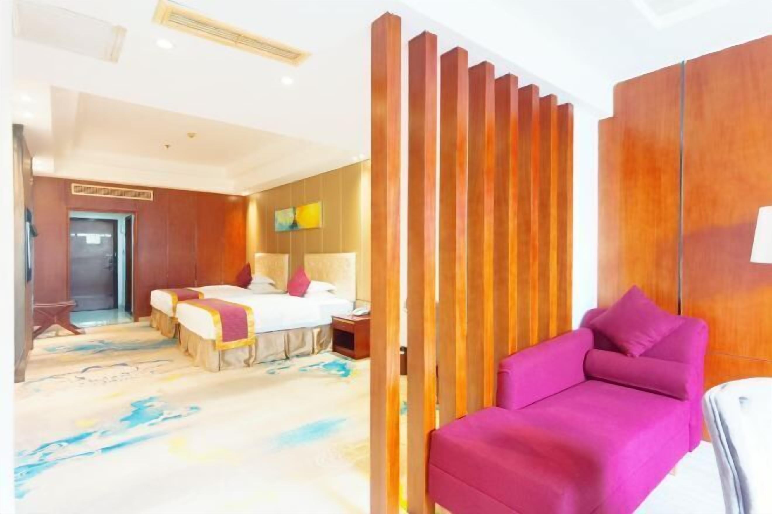A hotel room with a bed, a pink sofa, a wooden partition, and a carpet with a blue pattern.