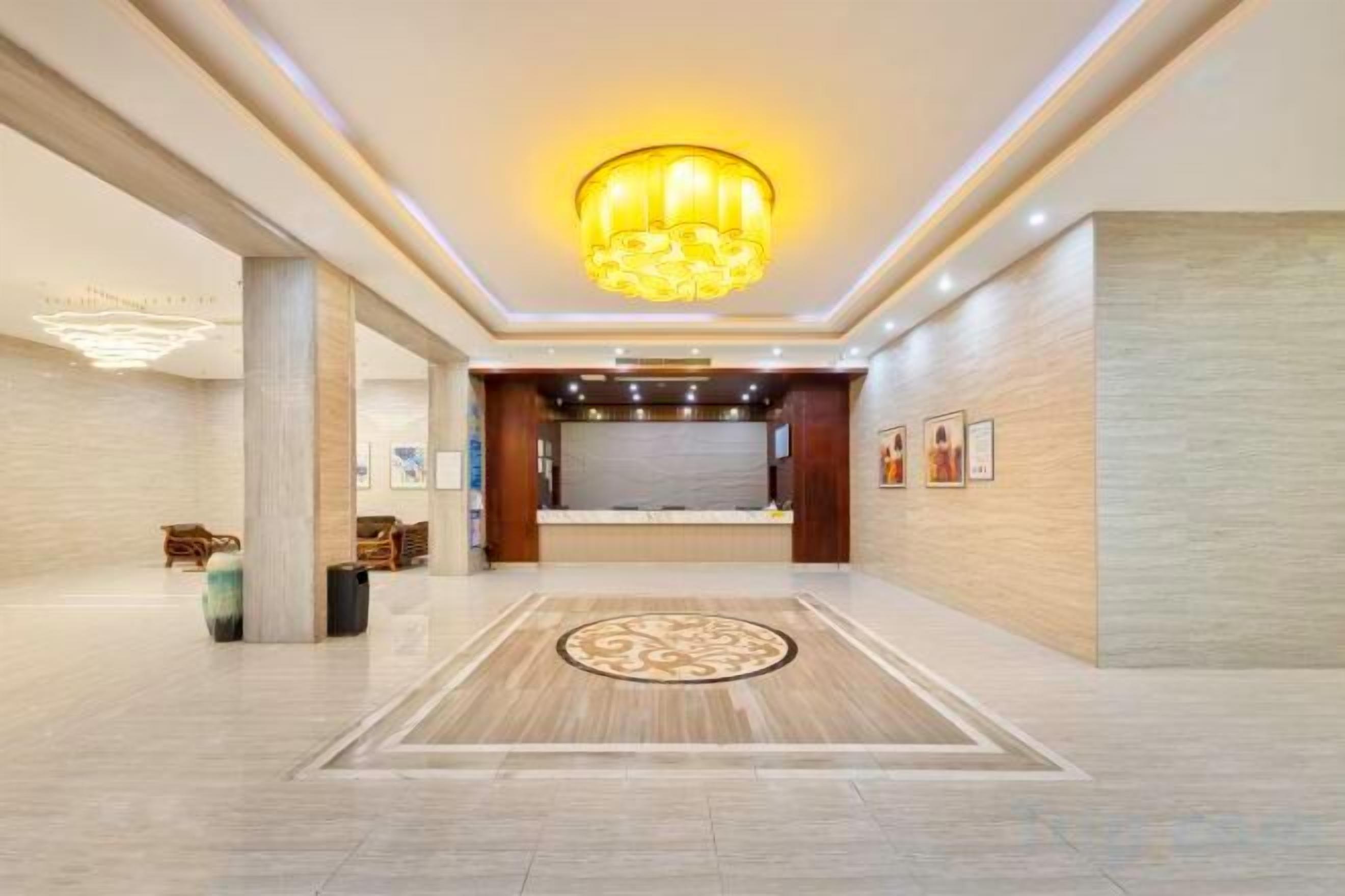 A hotel lobby with a reception desk, a chandelier, and a patterned floor.
